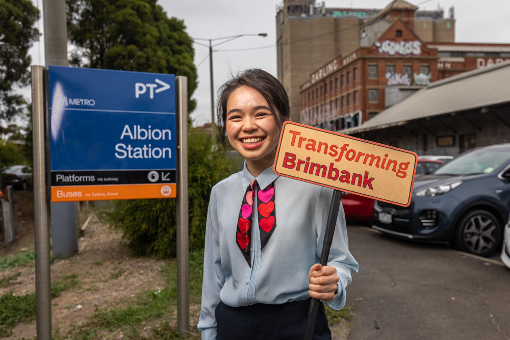 Cr Jasmine Nguyen stands in front of the Albion train station holding a sign that says Transforming Brimbank