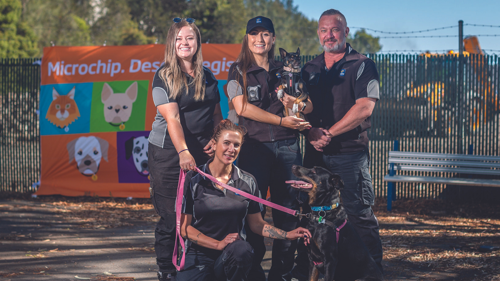 Five staff in brimbank uniforms post with dogs of different sizes. They arestanding in front of a banner about brimbank pet registration.