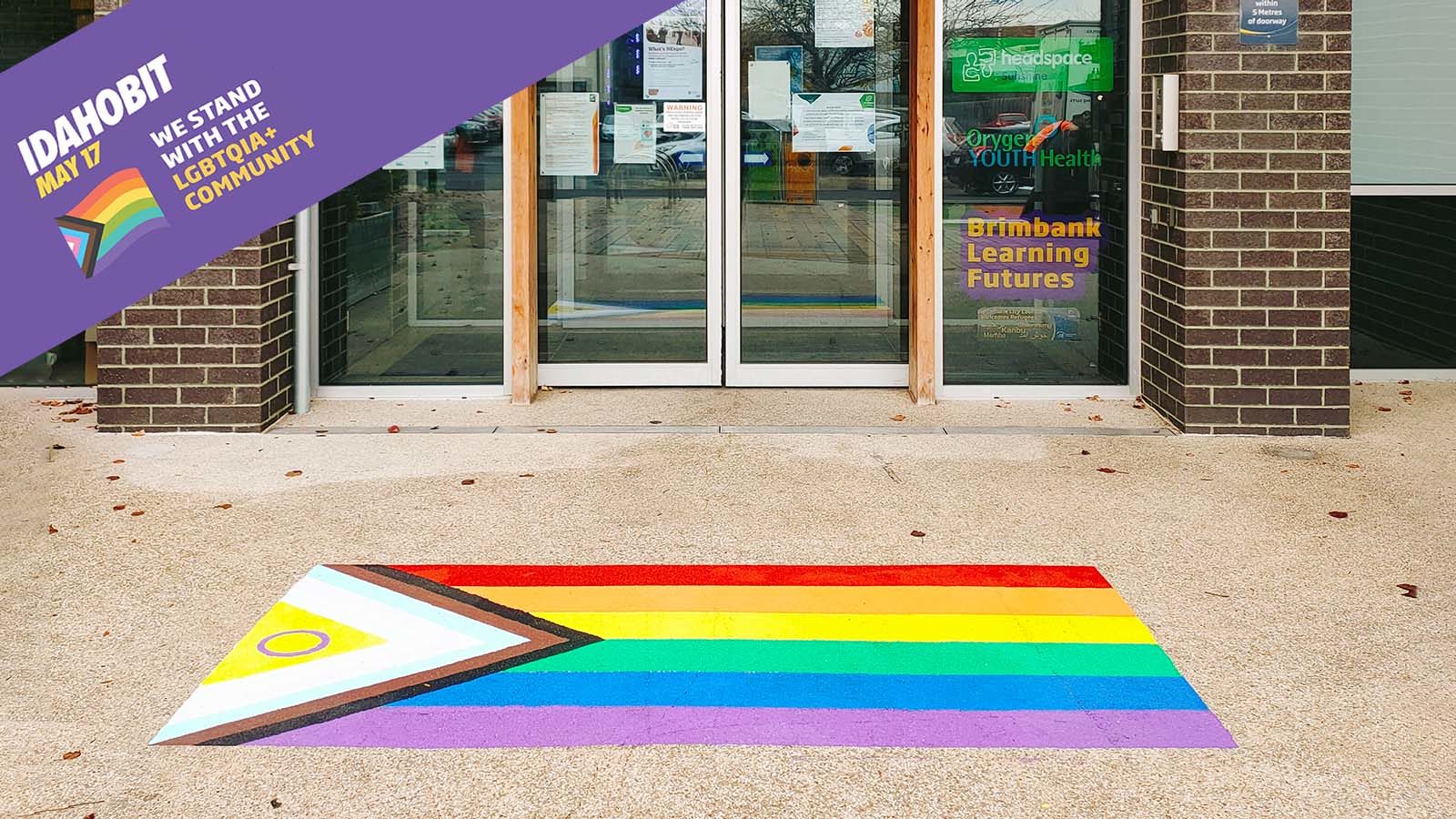 Pride rainbow flag on the ground in front of the doors to Visy Cares Hub. Message in top left corner: IDAHOBIT May 17 We stand with LGBTIQA+ communiities