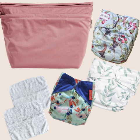 Several reusable nappies are laid out on a flat surface next to a nappy carry bag.